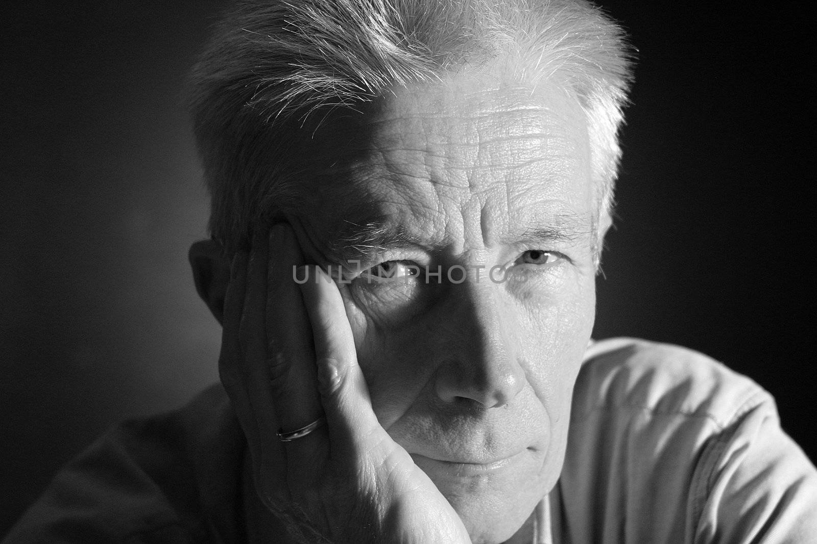 Good looking senior man leaning on his hand. Portrait taken in the studio over black