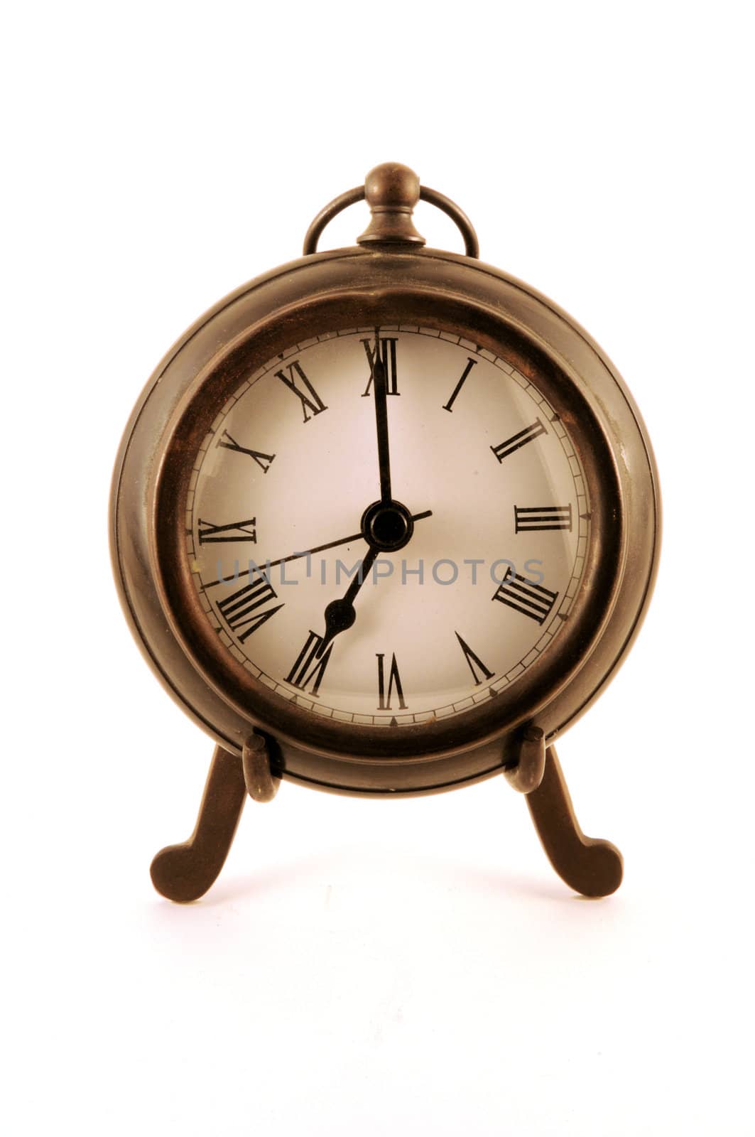 A round brass clock with roman numerals on a tripod stand reads seven o'clock.