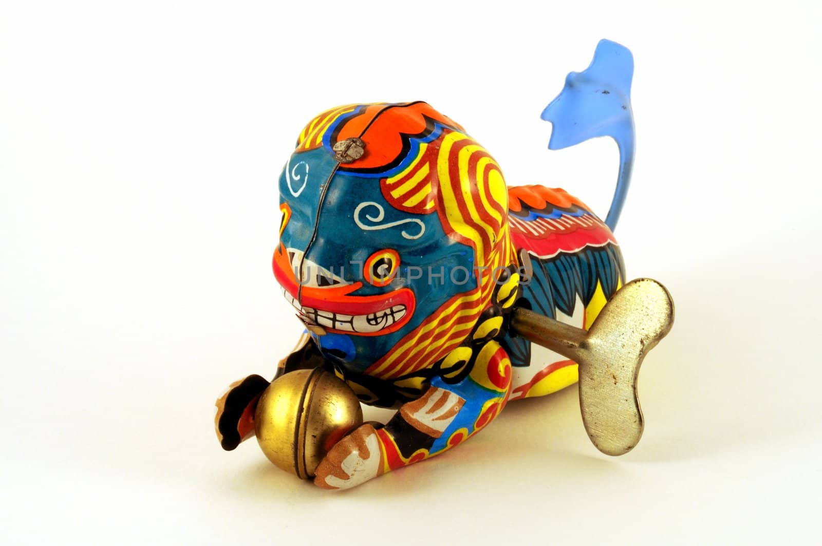 Wind-up toy dragon from China with blue tail and a golden ball in its paws, made of brightly-painted metal.  The winding key is visible in its side.


