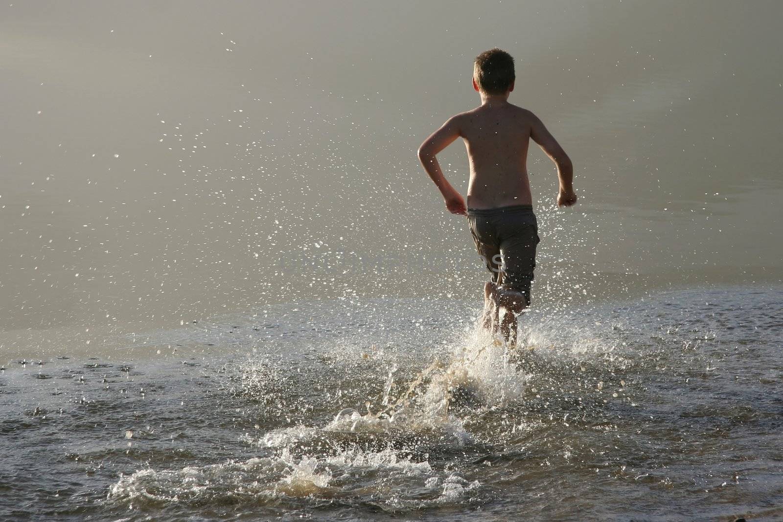 Young boy running in the shallow water of a river