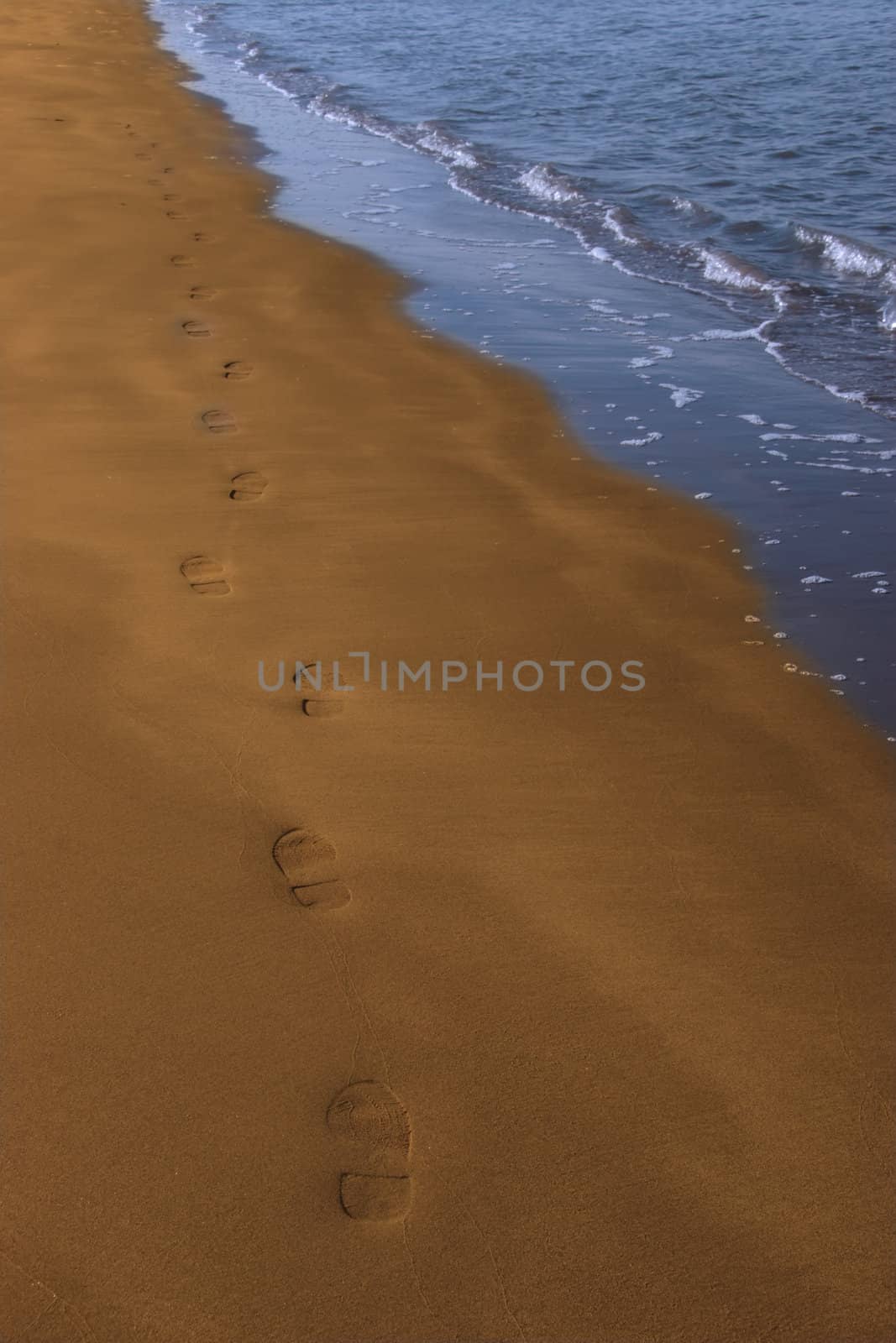 footprints left in the sand of an irish beach with the tide coming in