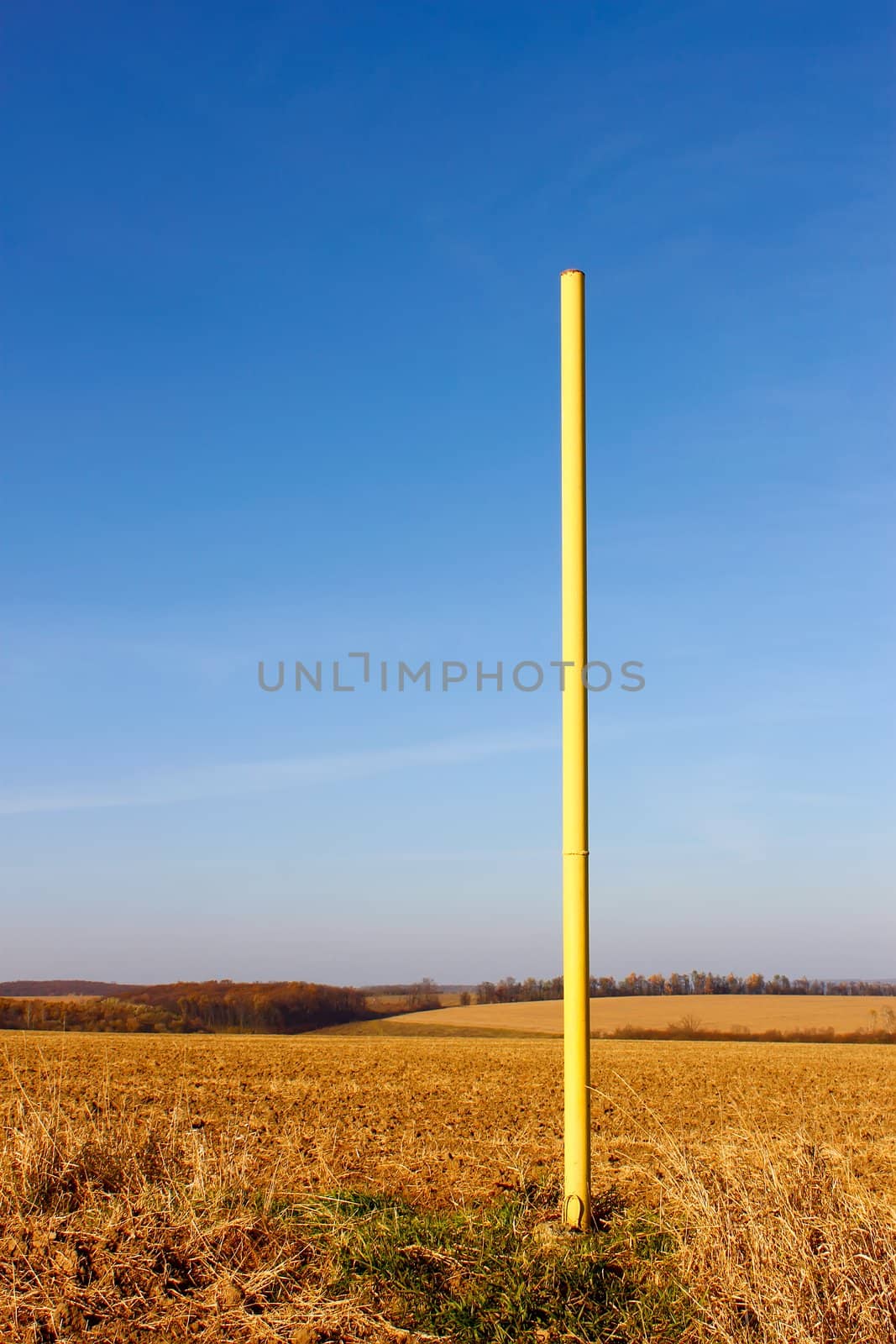 Yellow high iron pillar in the middle of autumn fields. Under ground pipeline laid