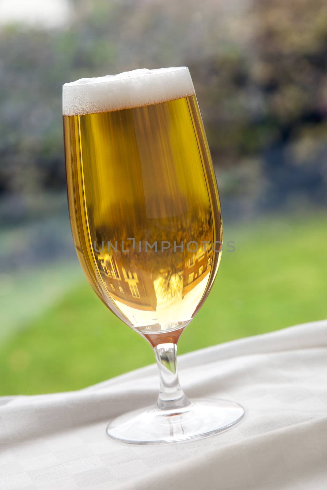 Recently poured glass of beer on a table in front of a window.