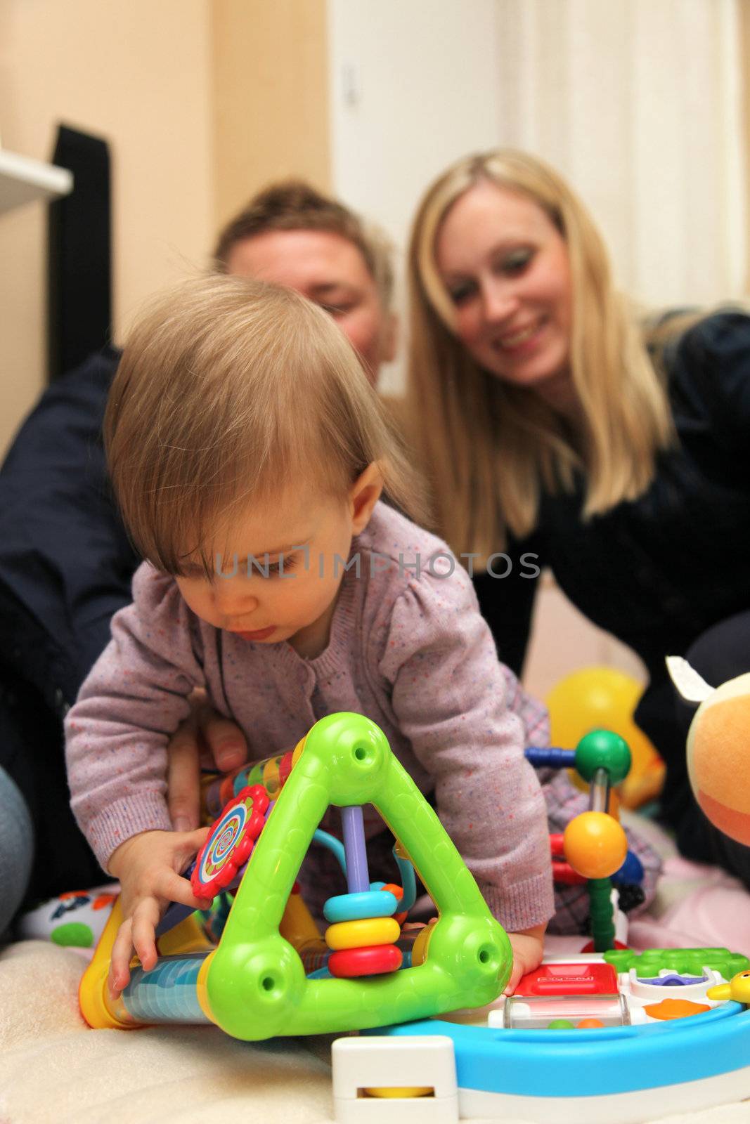 Happy little family with a child. The child plays in the foreground with Speilzeug, parents can be seen in the background

