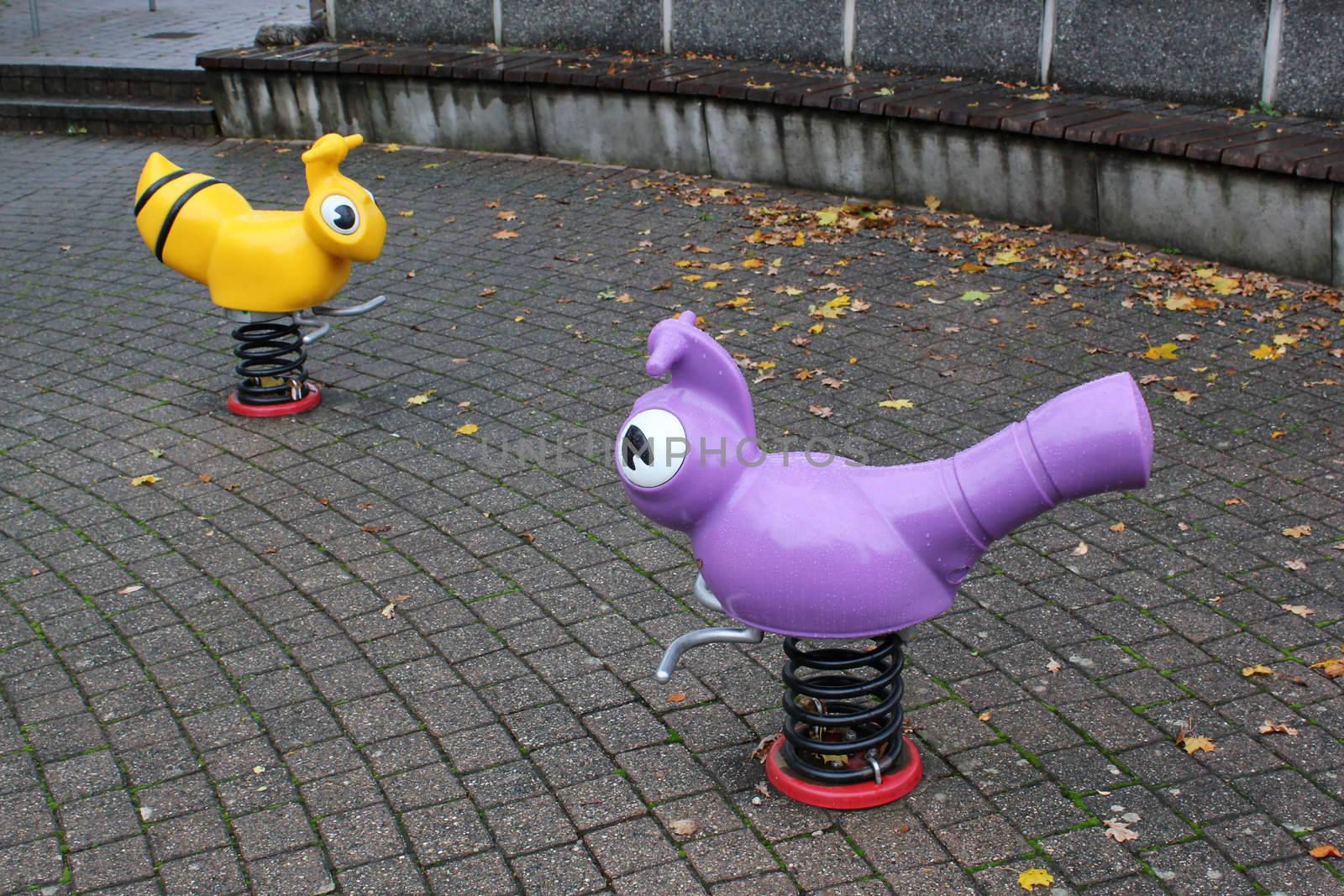 Playground for children with two plastic animals on springs by rainy autumn day