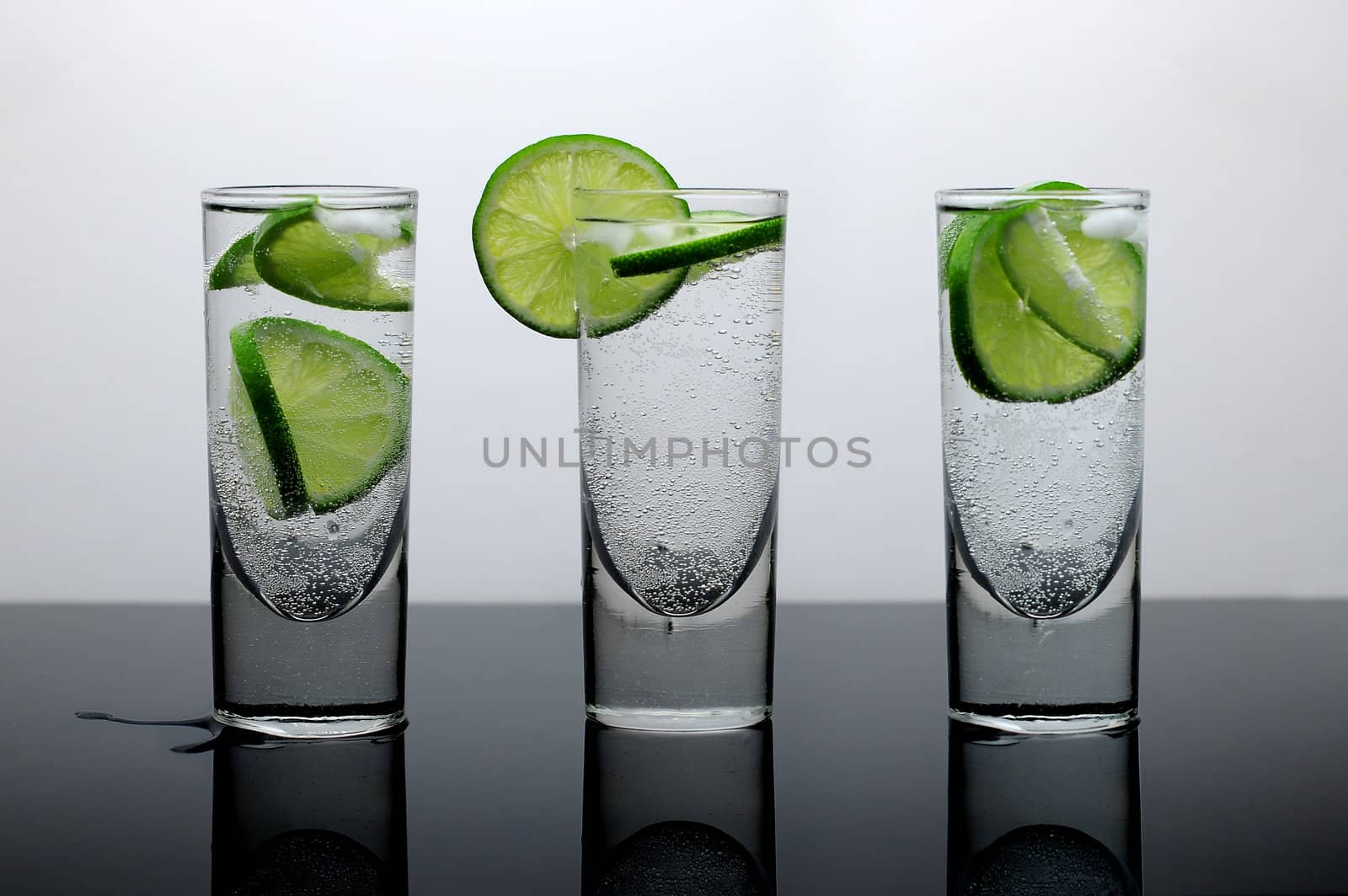 Fresh drink of water with lime and ice in three clear glasses on a reflective surface