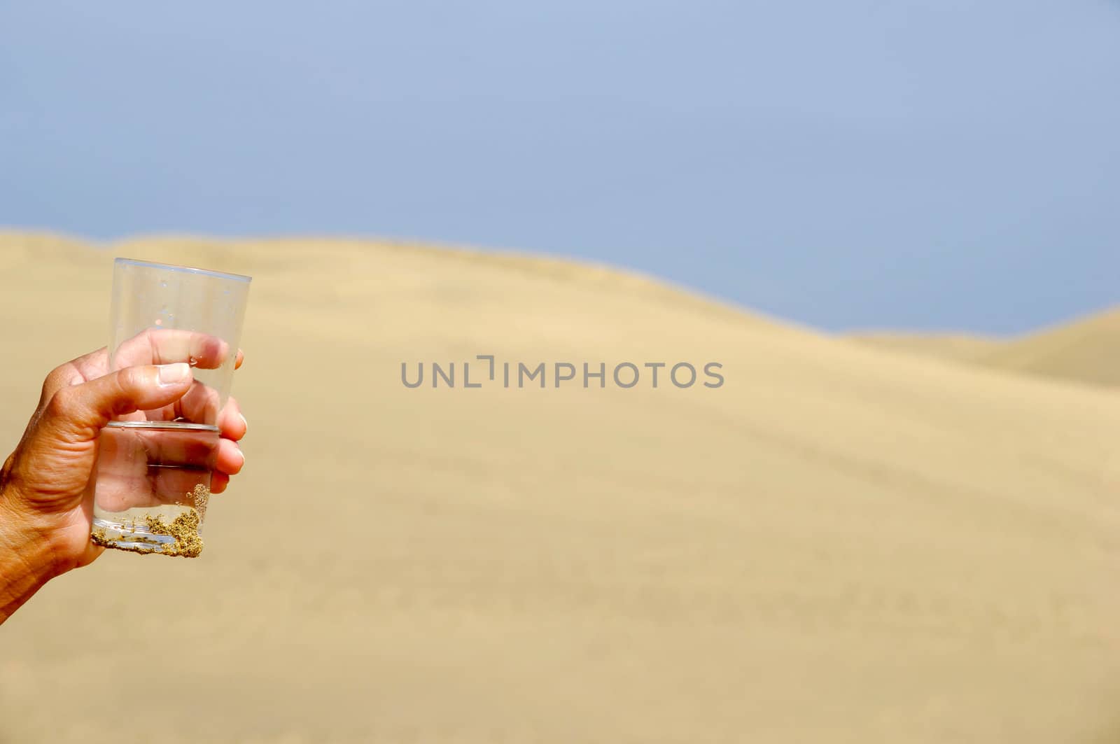 Hand is holding a fresh glass of cold water in desert.