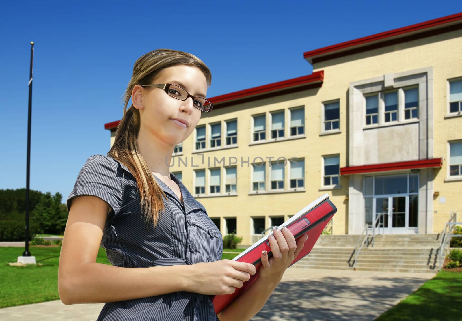 Back to school: confident young female student with books in front of school entrance. Could be college or small university campus.