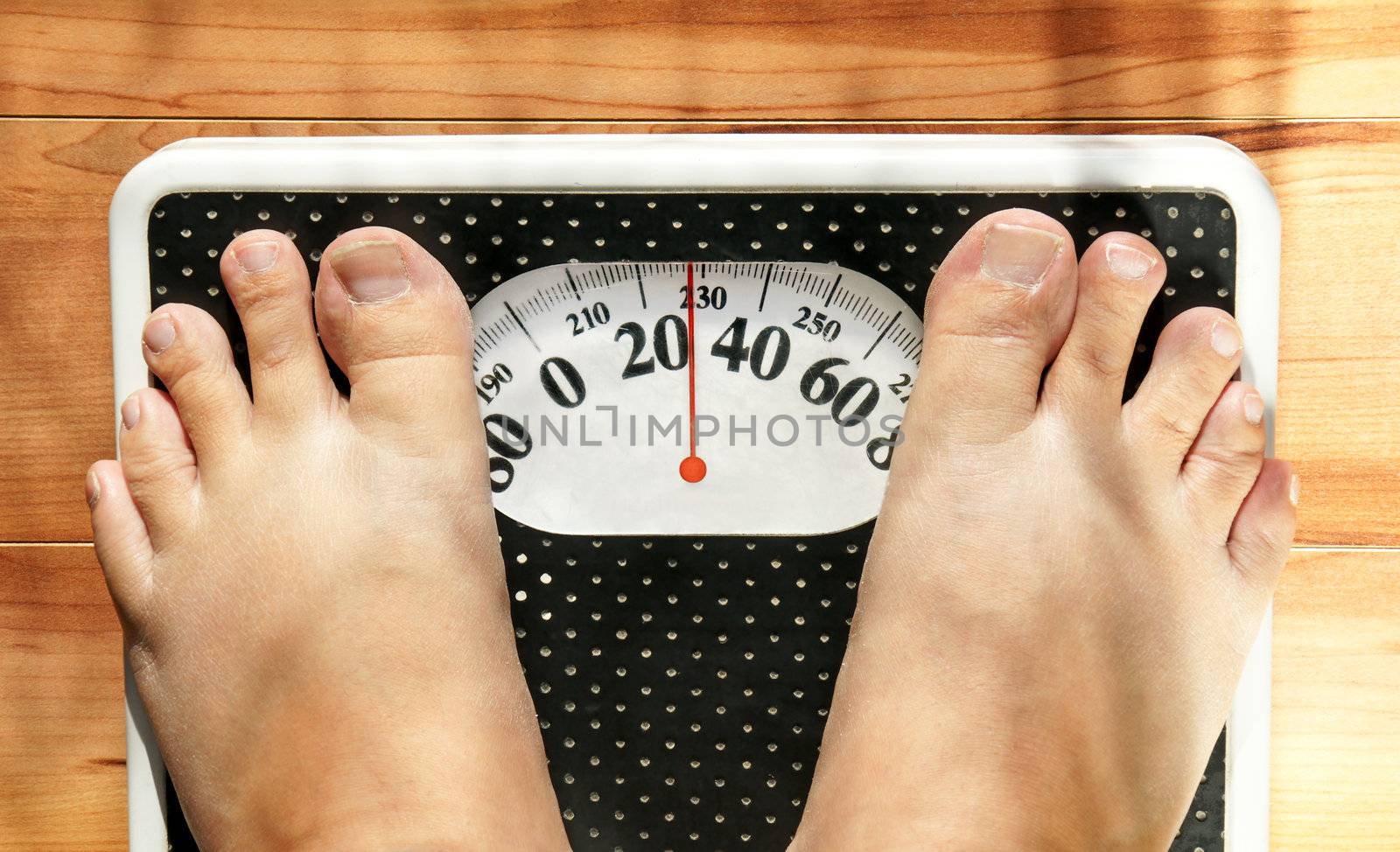 Feet of a fat person on a weight scale (measuring both in pounds and kilograms) showing obesity.
