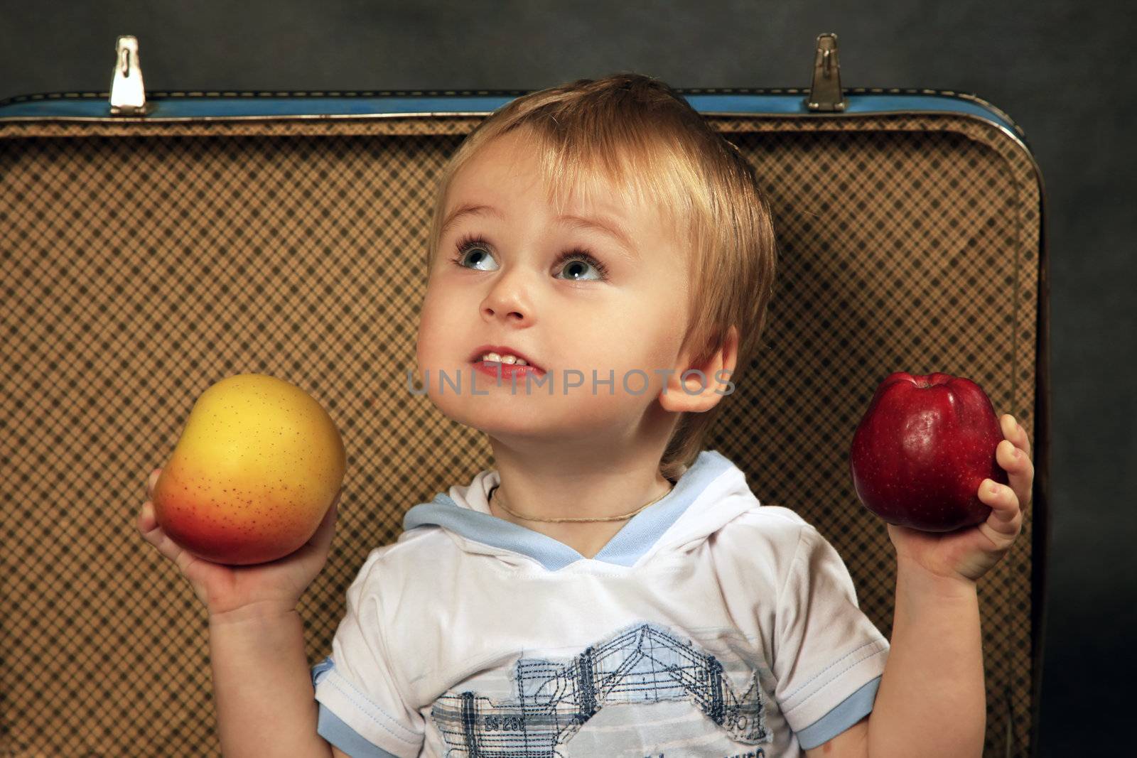 The little boy with a apples sits in a old suitcase