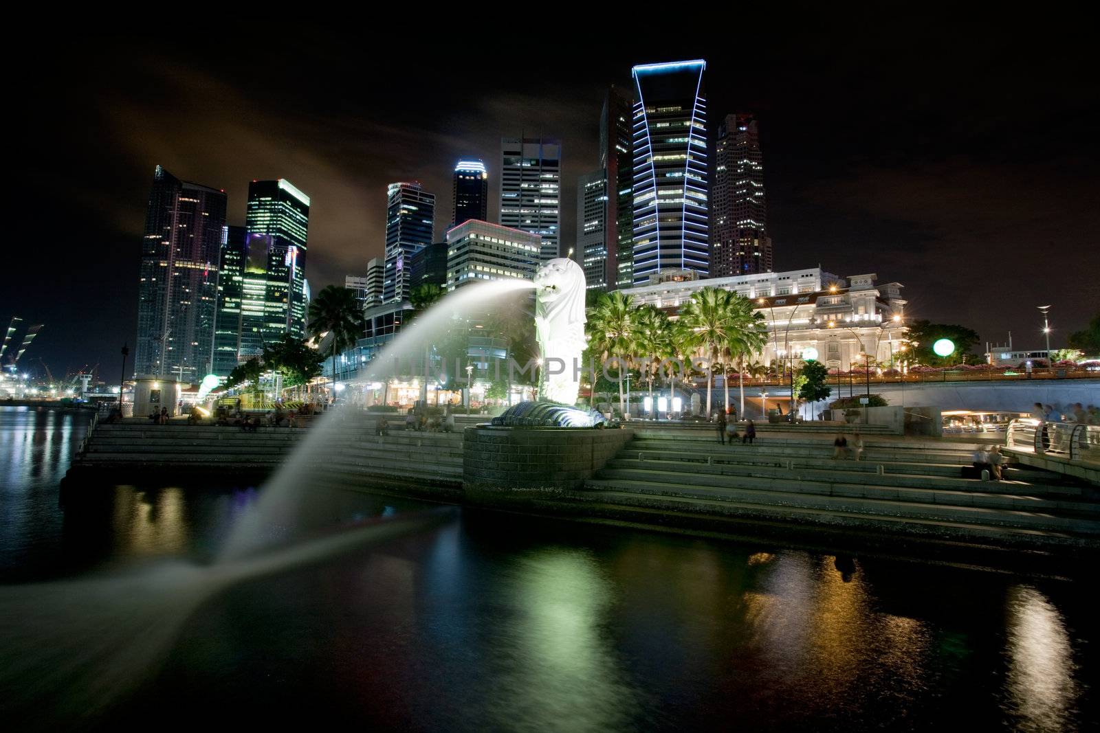 A view of singapore at night with the merlion in the foreground