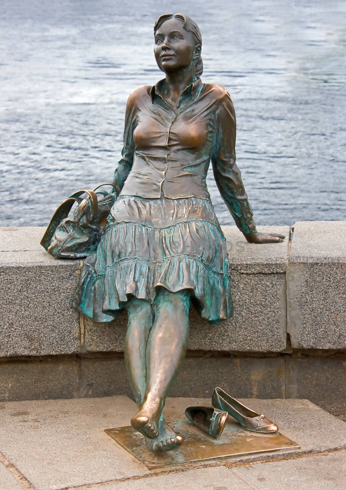 Sculpture of a girl sitting on the parapet on the background of the river, Novgorod, Russia.
