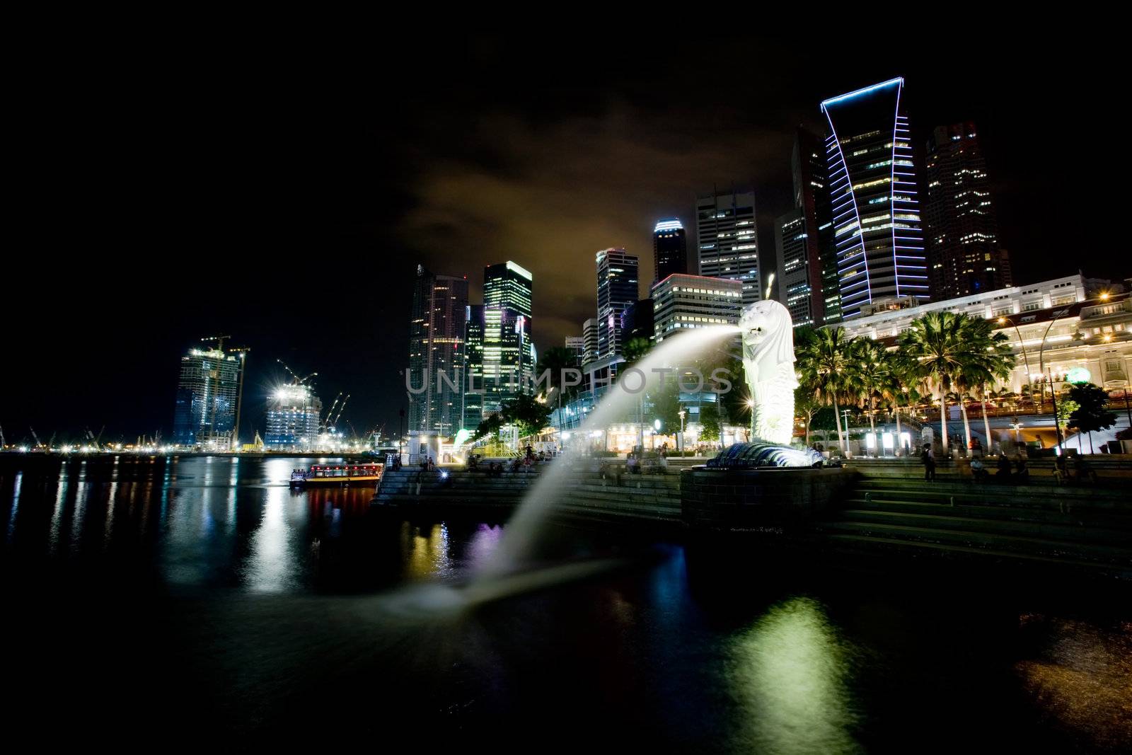 A view of singapore at night with the merlion in the foreground