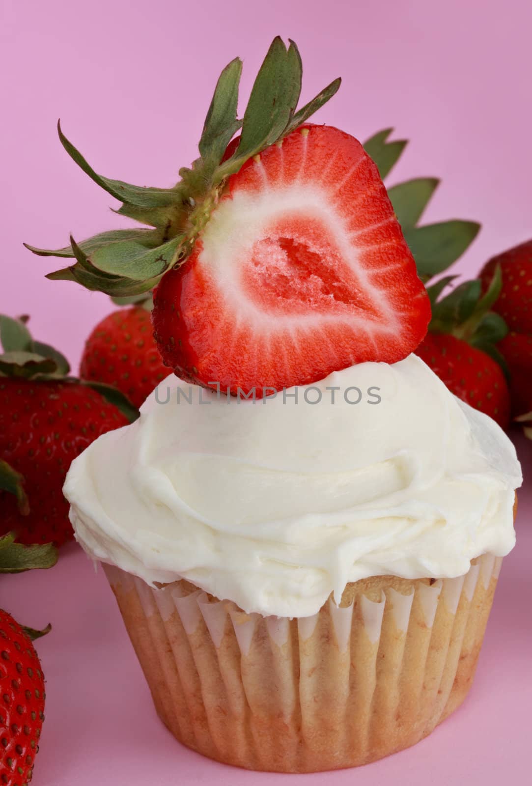 cupcake with white sugar icing and strawberry, pink background