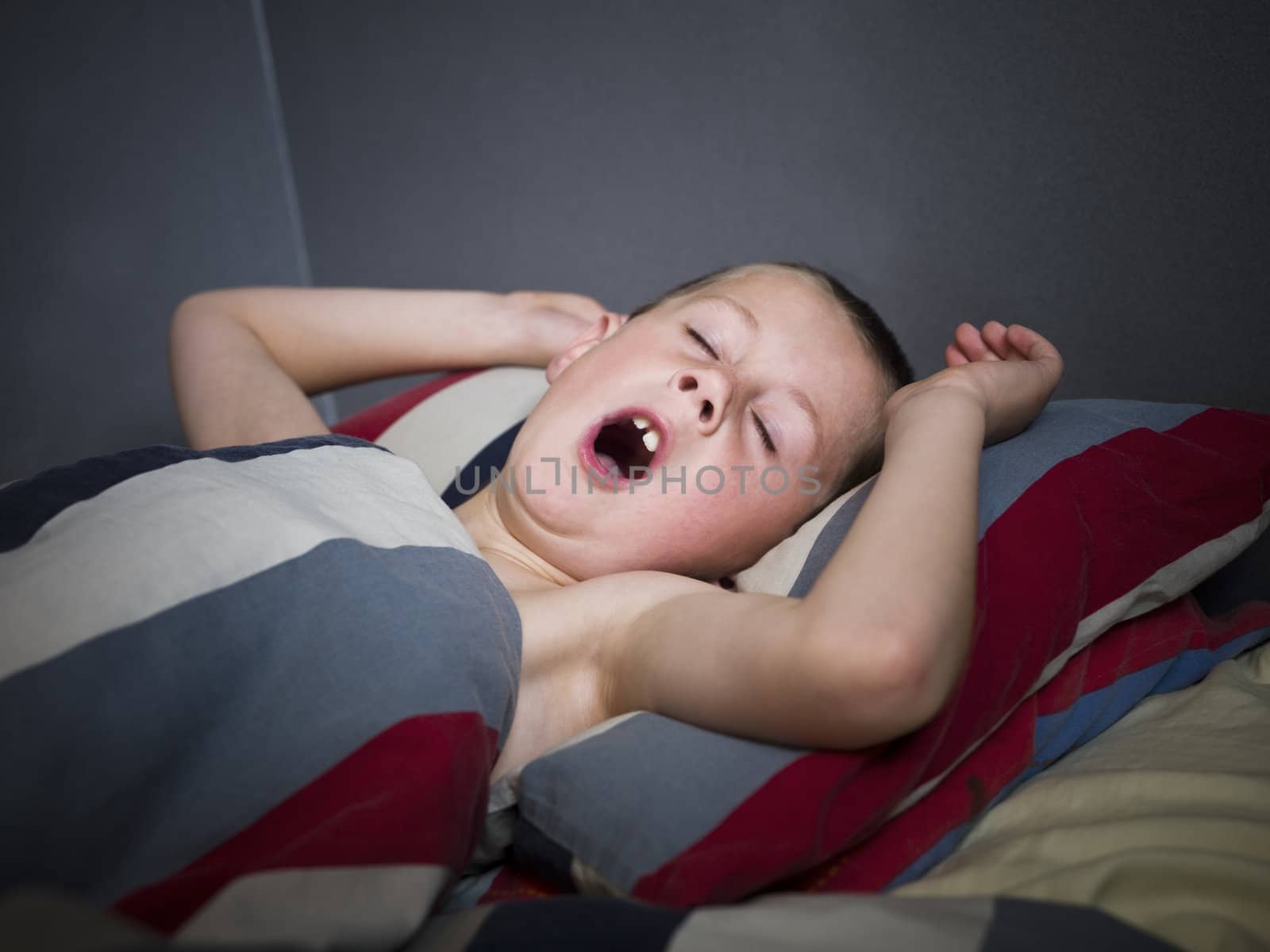 Young boy yawning, lieing in his bed