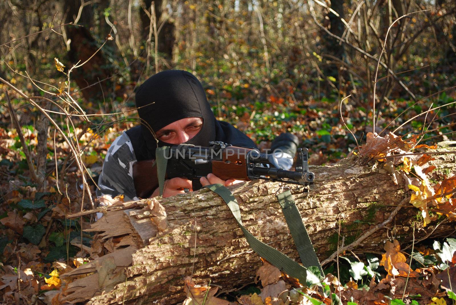 terrorist in camouflage aiming with his rifle outdoor in forest