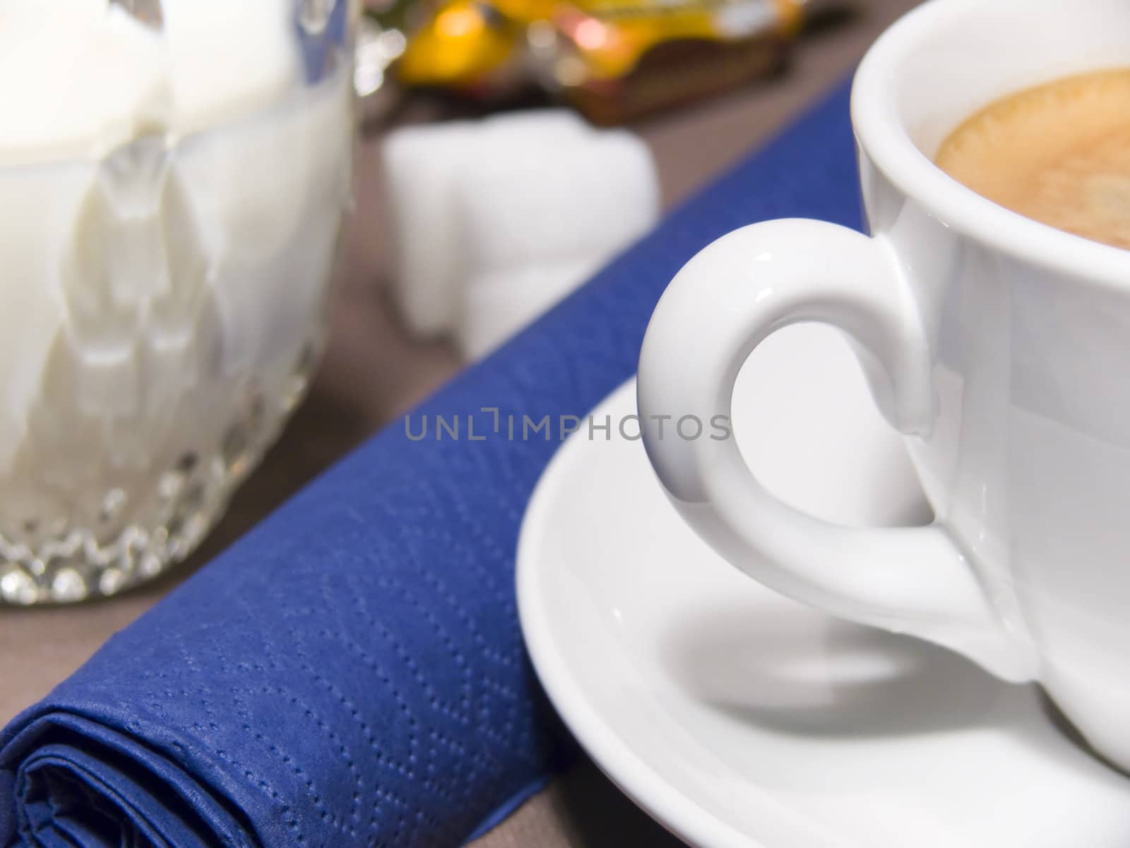 A cup of coffee with foam, milk, sugar and a blue napkin