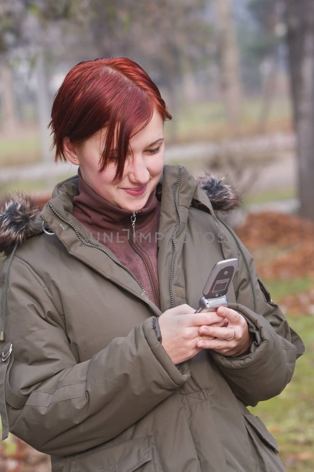 Redhead teen girl checking her mobile phone in an autumn park.Shot with Canon 70-200mm f/2.8L IS USM.