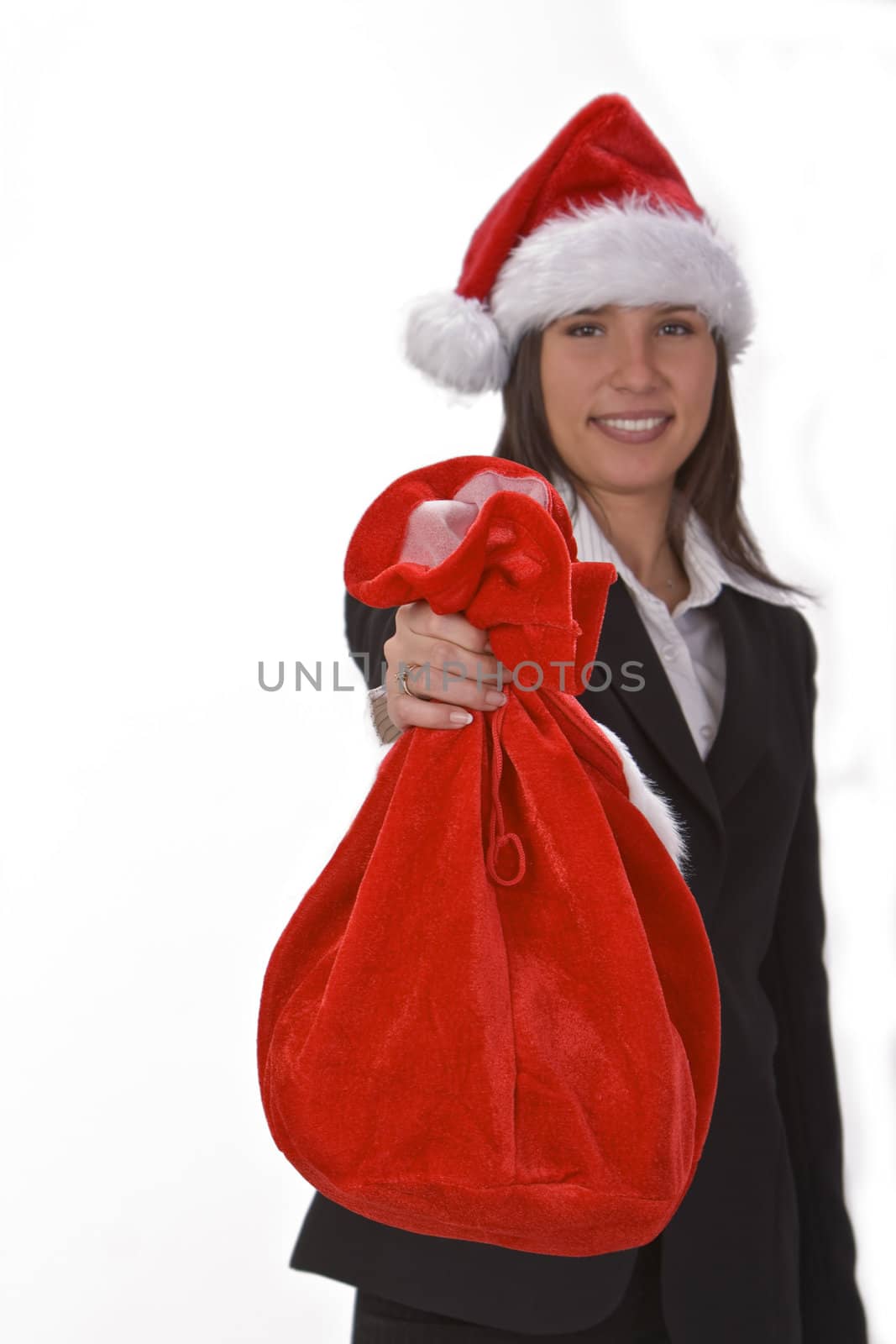 Young businesswoman wearing a Santa's hat and offering a red sack full of gifts.The focus is selective on the sack. 