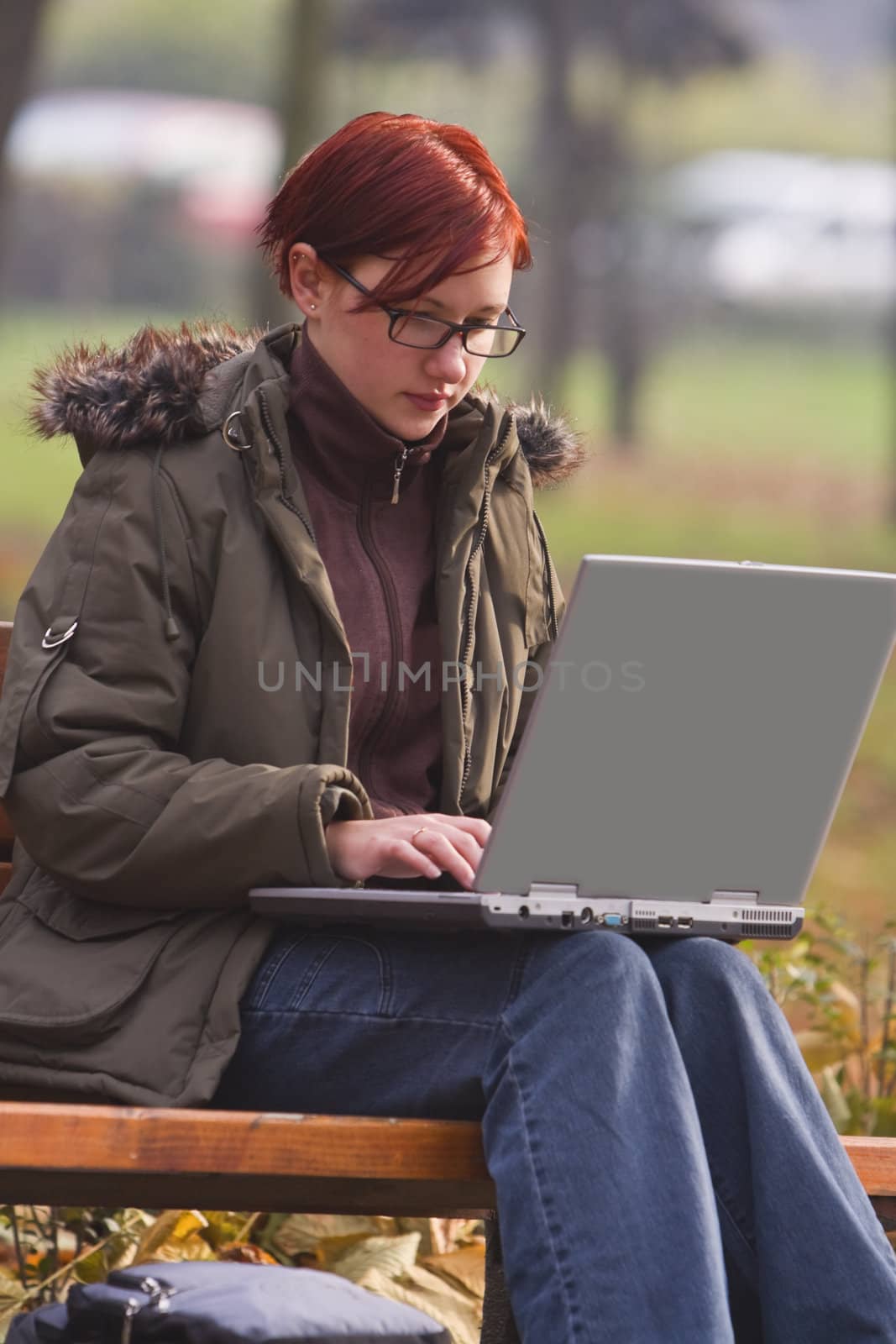 Redheaded girl working on a laptop in an autumn park.Shot with Canon 70-200mm f/2.8L IS USM