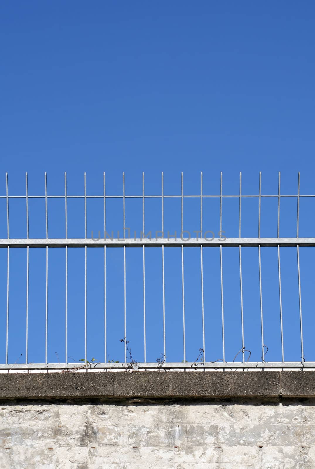 Metal fence on a concrete railway bridge against a clear blue sky. 
