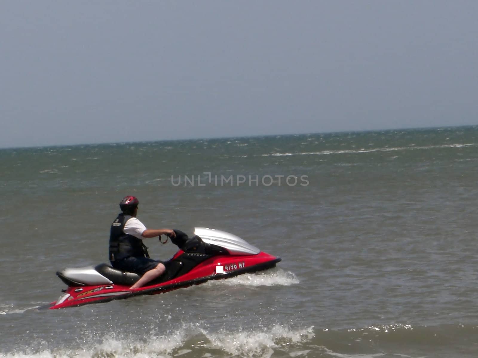 A man is wearing a safety vest and is riding a jetski in the ocean.