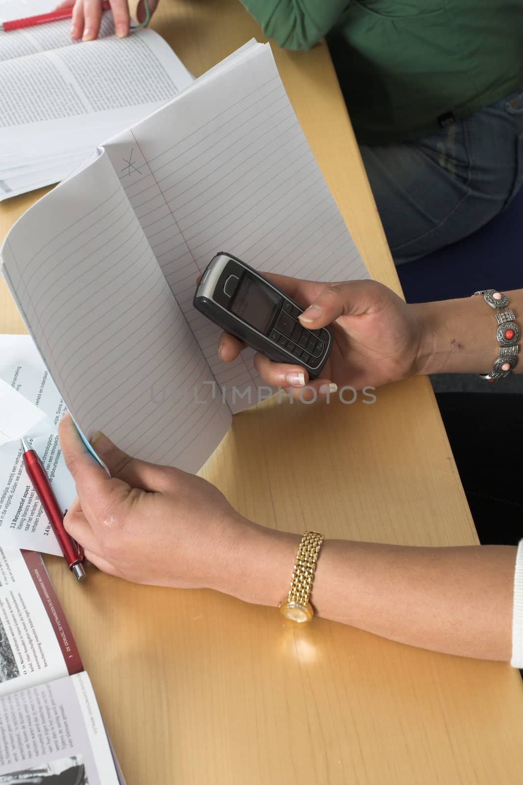 Girl in a school environment sending a text message hiding behind her notebook