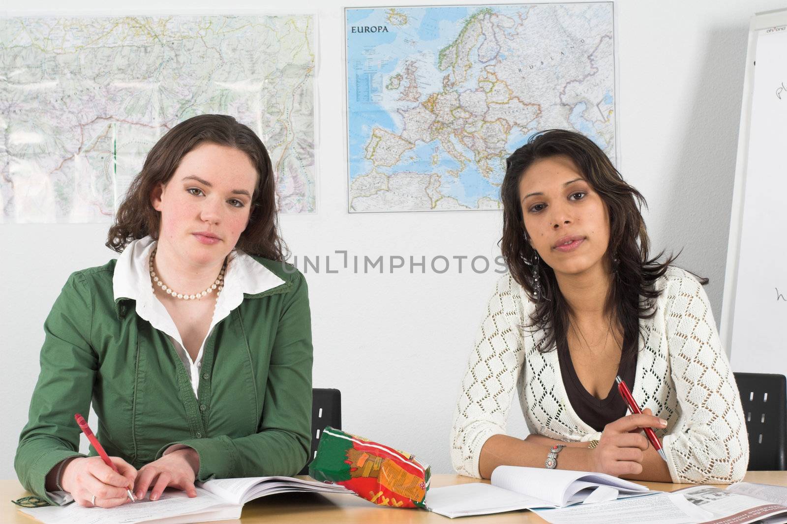 Two girls in a classroom looking very attentively to the teacher