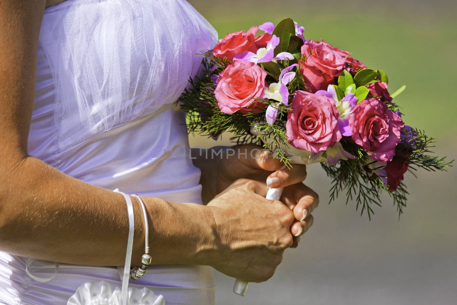 A closeup shot of a bride holding a beautiful bouquet of red and pink flowers on her wedding day
