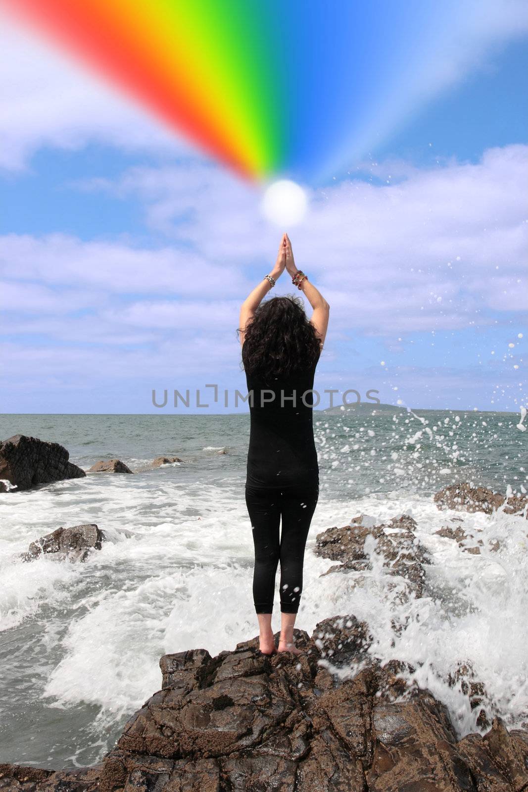beautiful woman on the edge of the rocks with waves splashing with ball of energy emiting rainbow