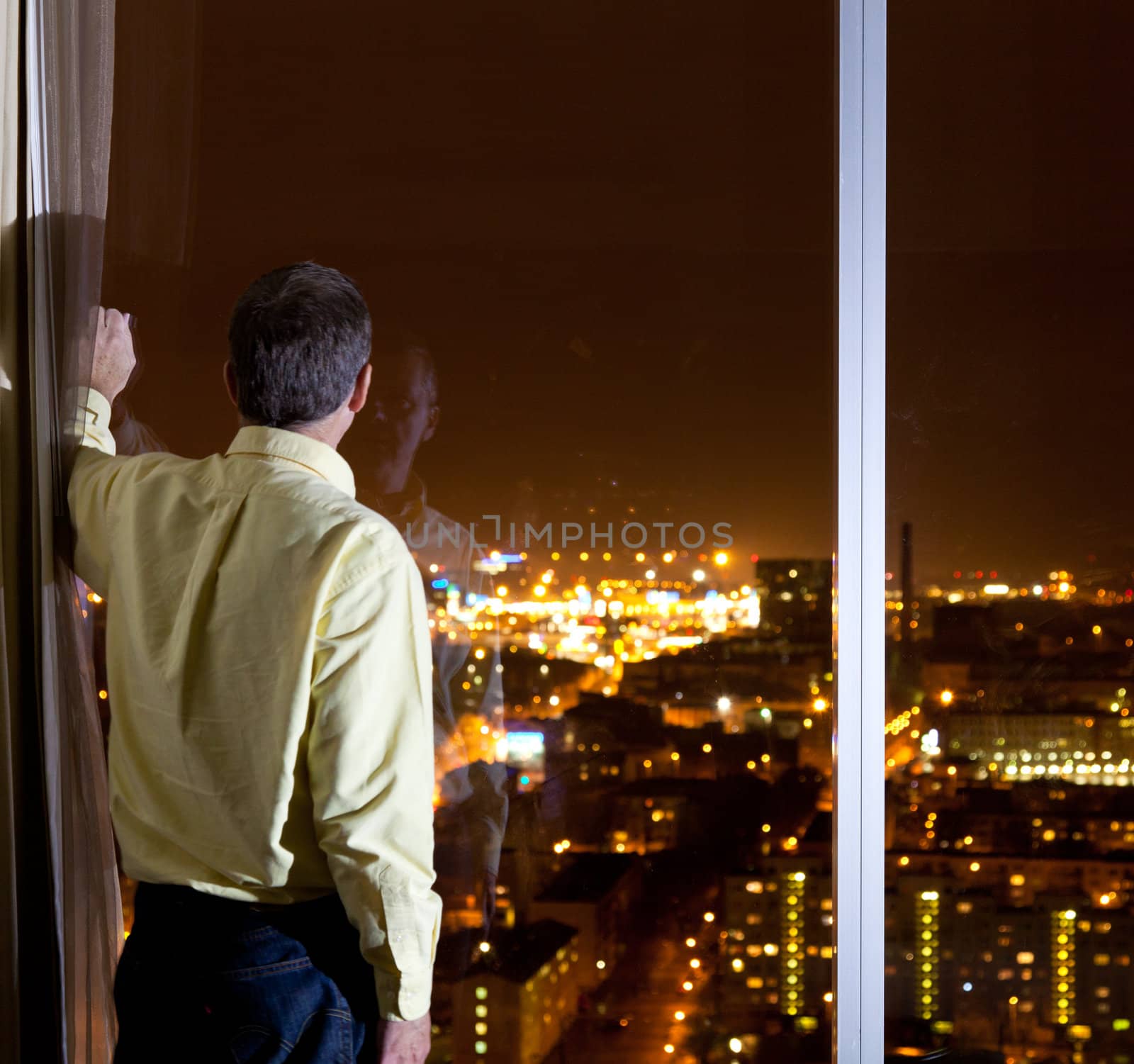 Middle aged man looking out over a city from a high window in a hotel or office