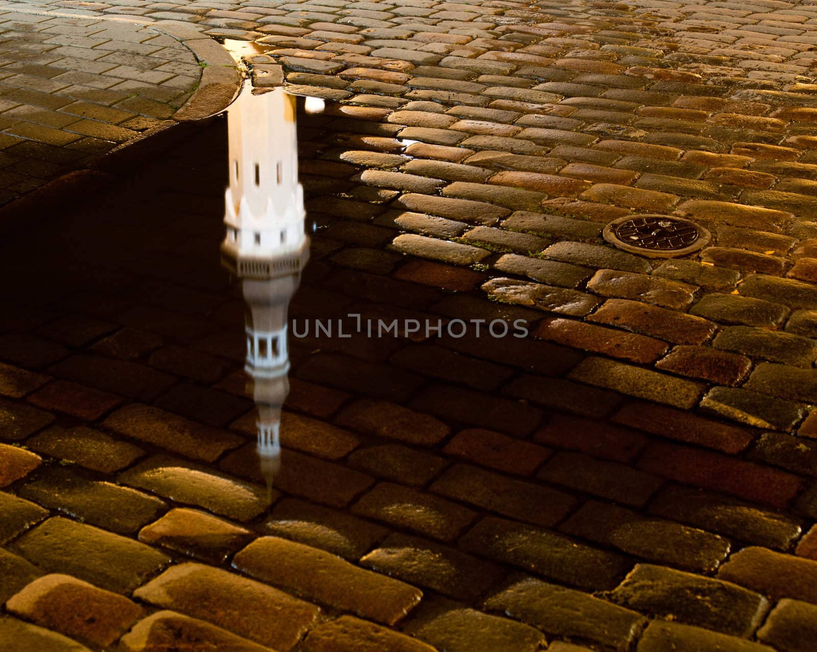 Tallinn town hall at night in Raekoya square showing the floodlit spire and tower of the hall reflected in a rain pool on the cobbled streets