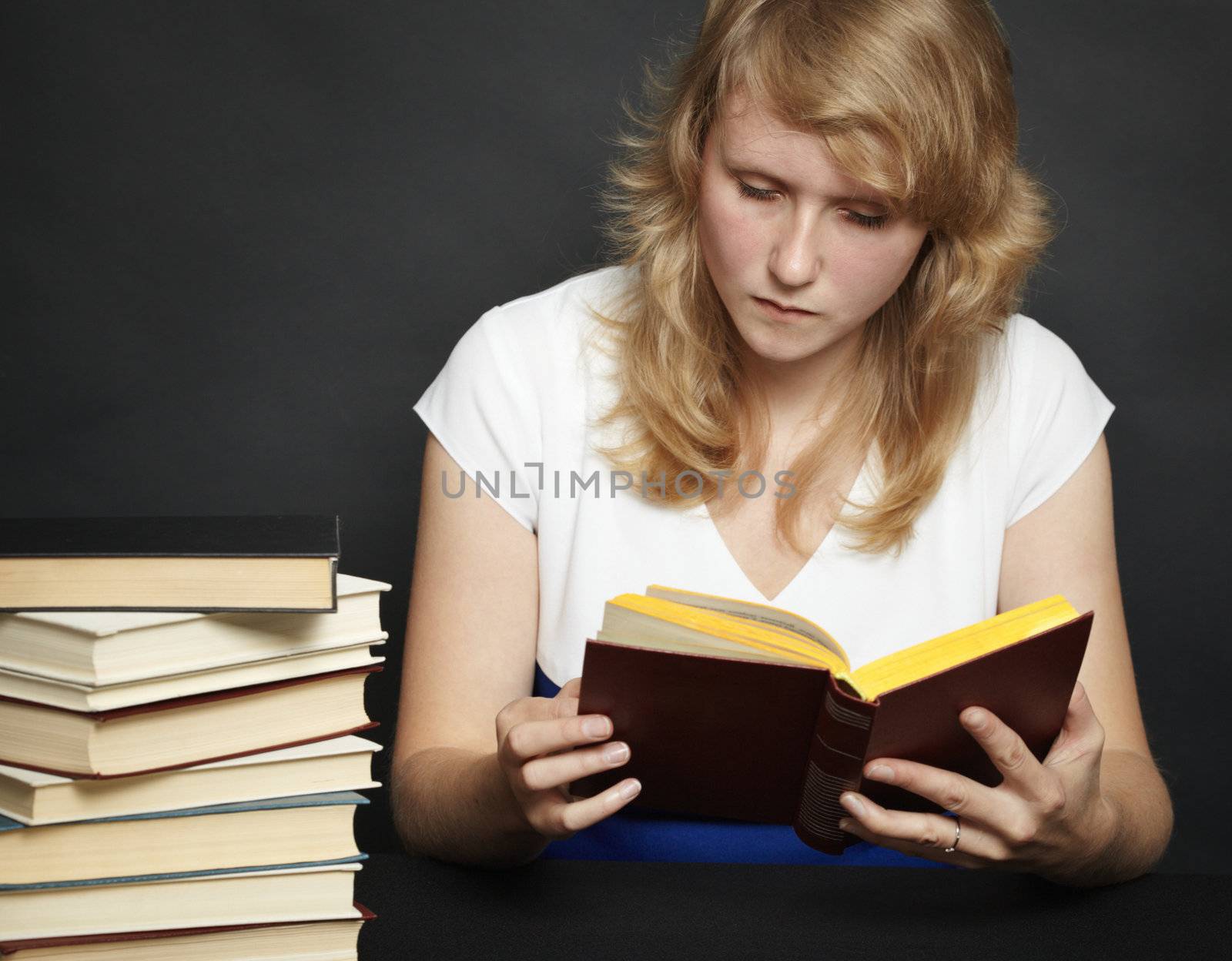 The young woman attentively reads the book against a dark background