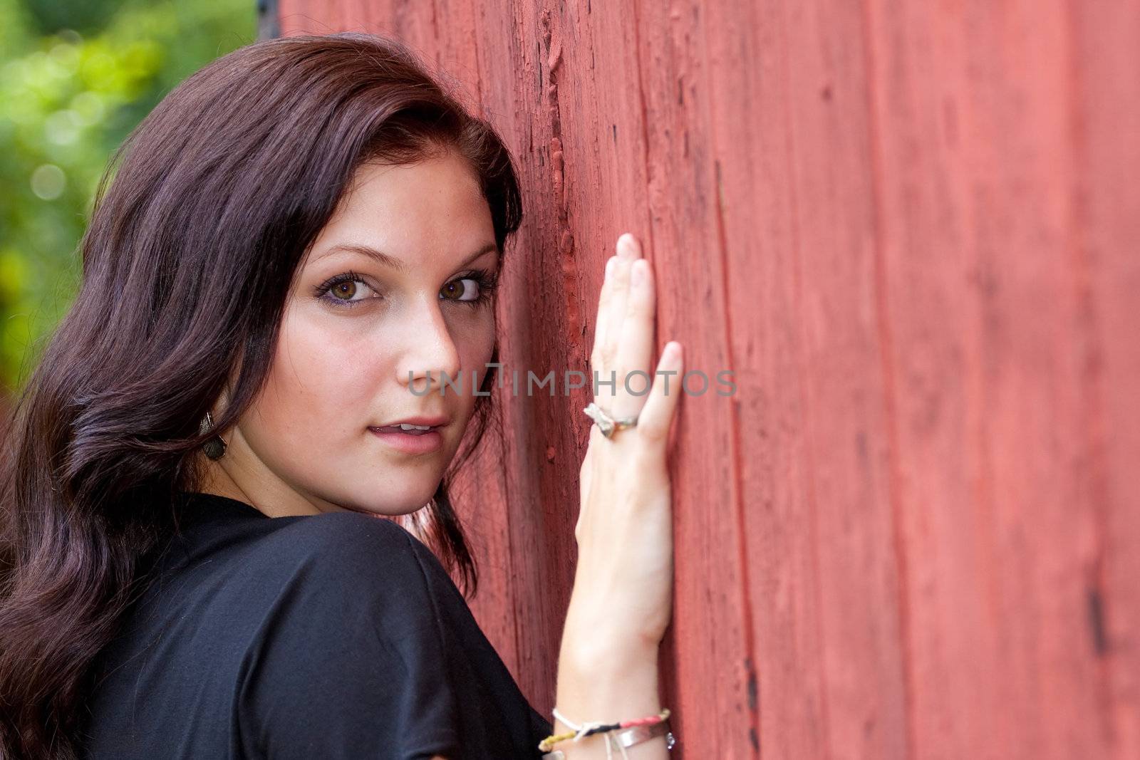 A pretty young woman in a black dress leaning against an old red doorway. 