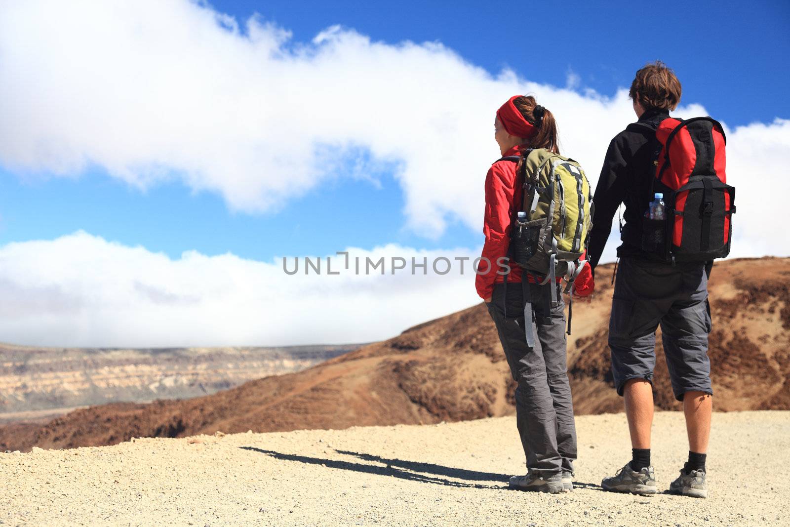 Hiking couple looking at the view holding hands in Teide National Park, Tenerife -  Copy space. Image from the volcano on the hiking path to Montana Blanca.