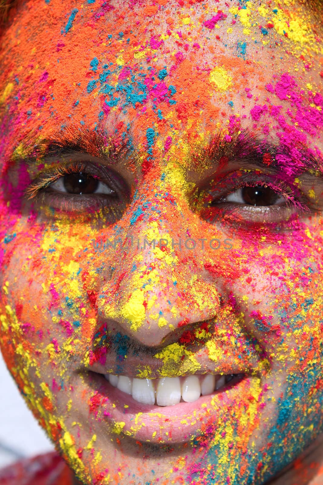 A portrait of a young Indian man with his face covered with colored powder, during holi festival.