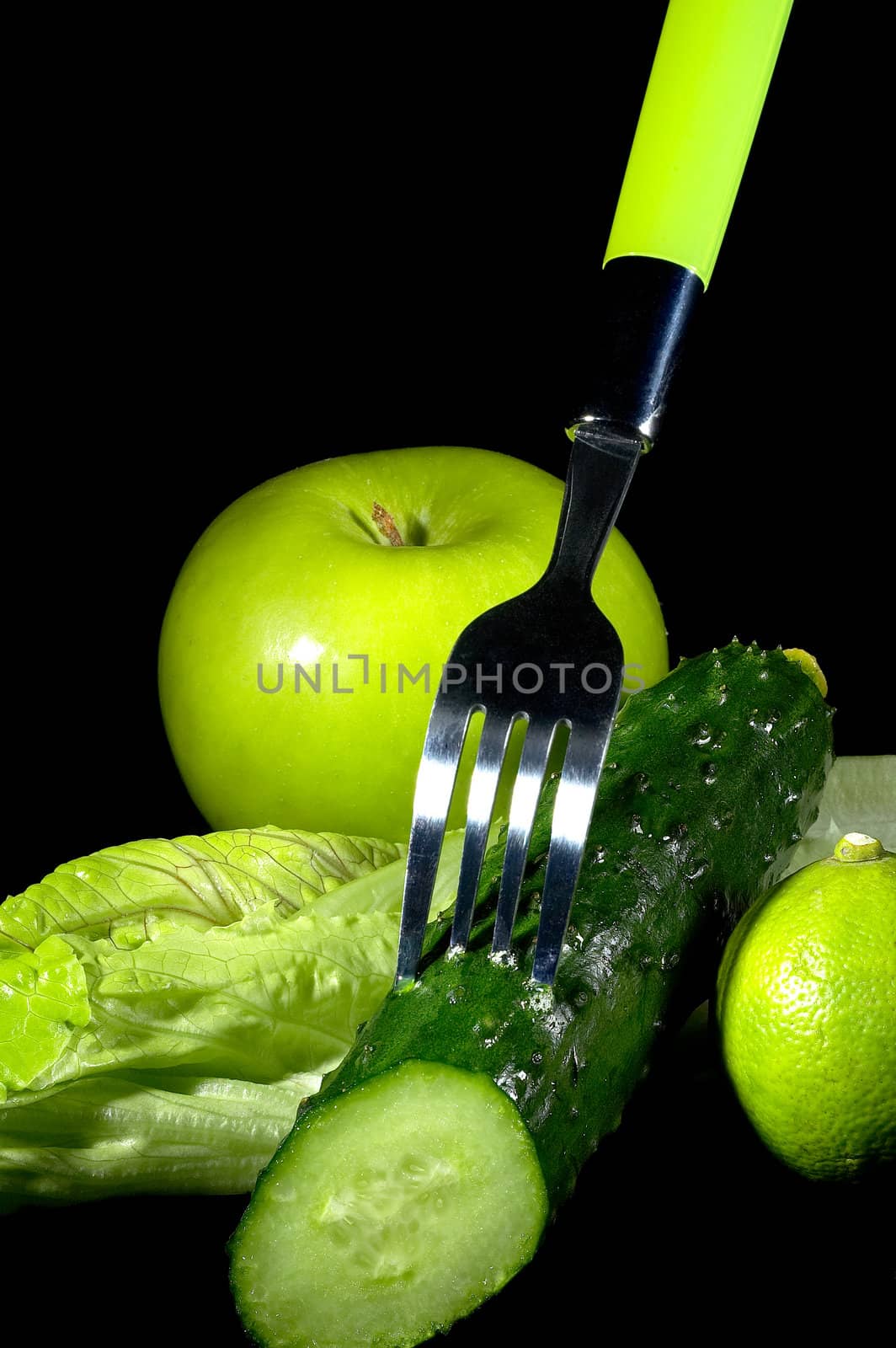 group of green vegetables and fruits with fork over black background