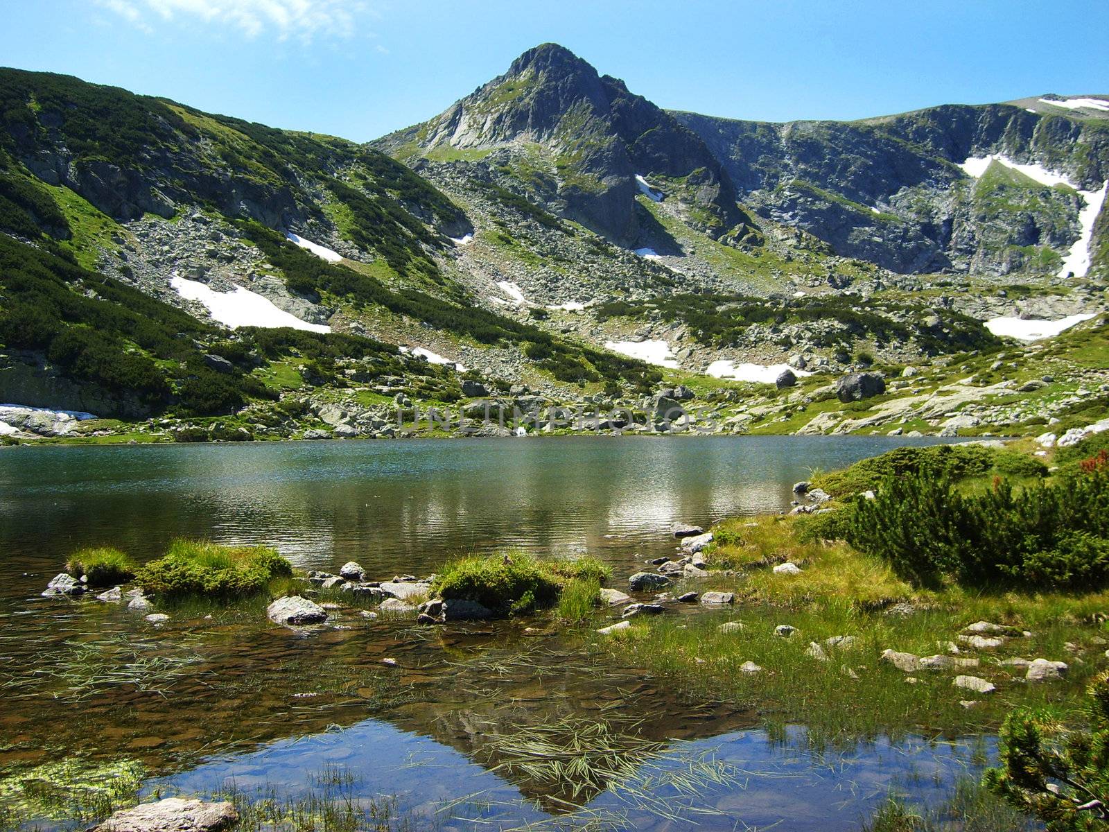 green rock mountain reflected in clear lake