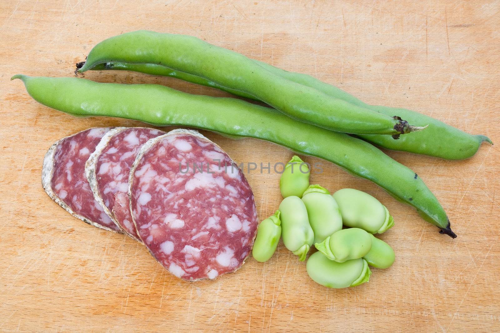 Three salami slices with fava beans on a wood chopping board