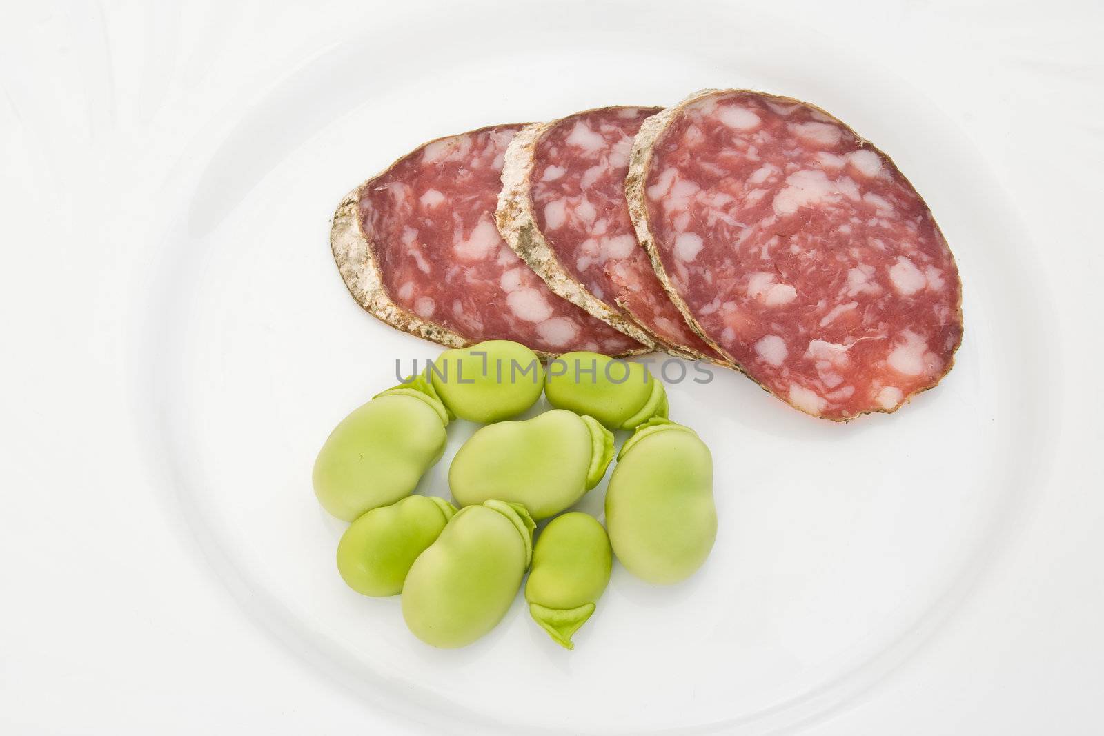 Three salami slices with fava beans on a white dish