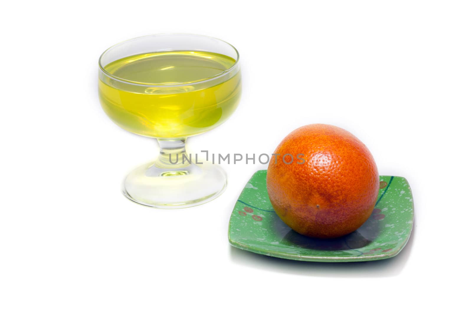Yellow jelly but transparent glass and orange on green saucer on white background