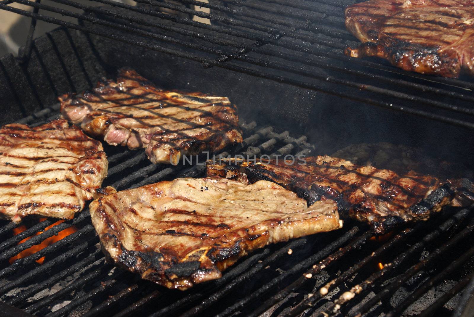 Several rib steaks grilling on the BBQ.