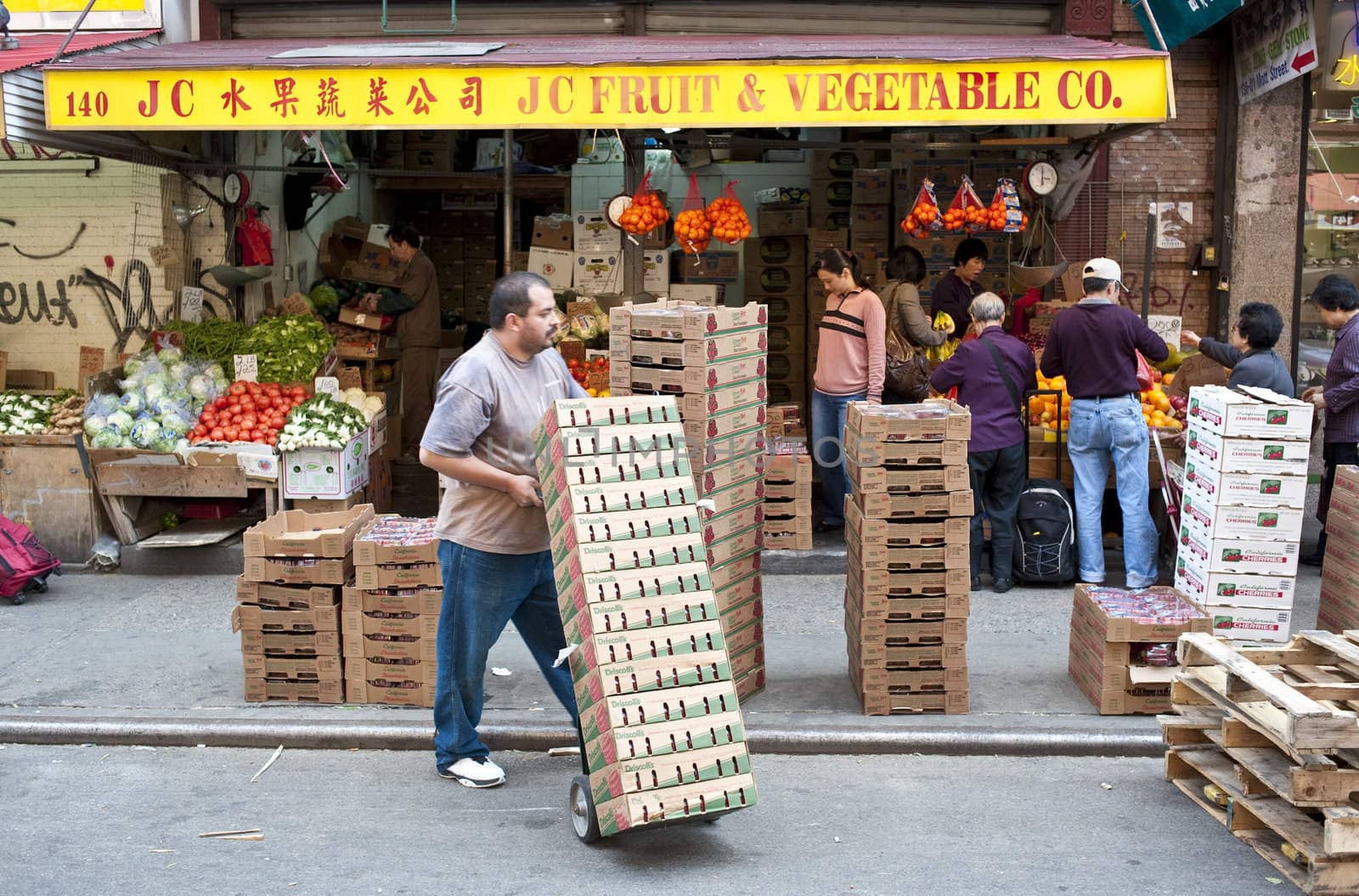 Man with hand truck of produce boxes in front of Chinese produce shop, chinatown, NYC