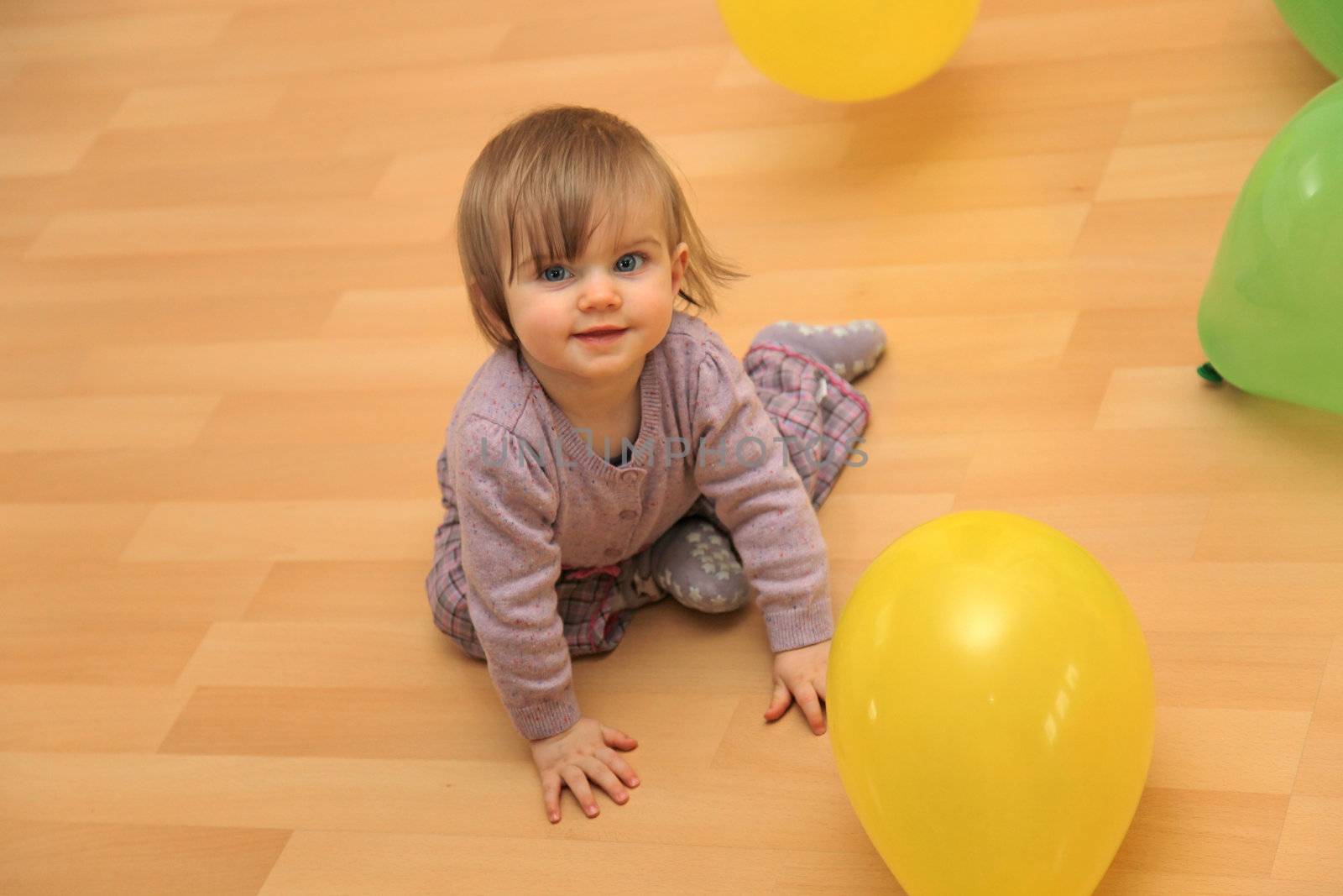 Happy little child playing with balloons. It sits on the floor and looking towards camera
 