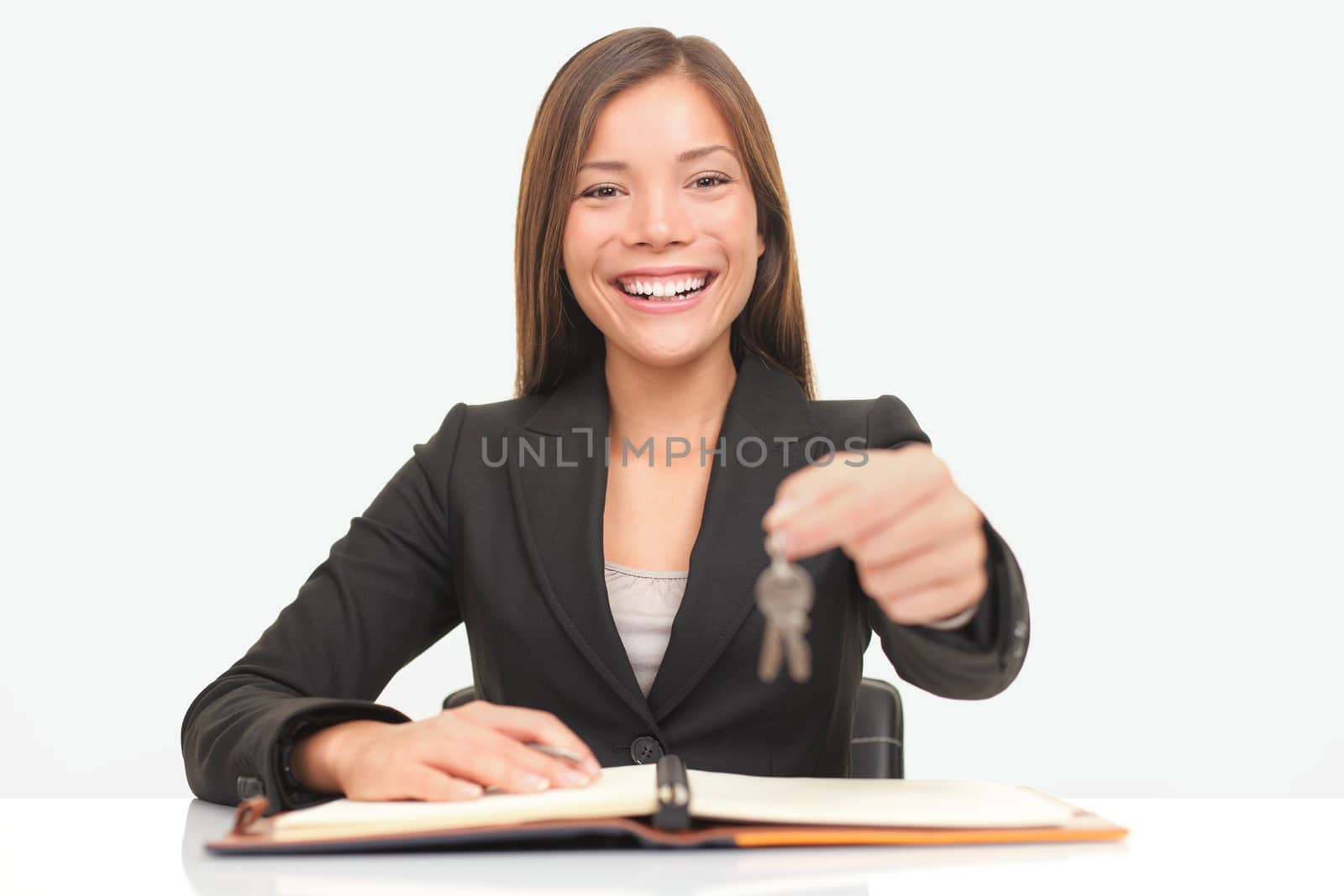 Real estate agent sitting at desk giving house keys smiling to new home owners.