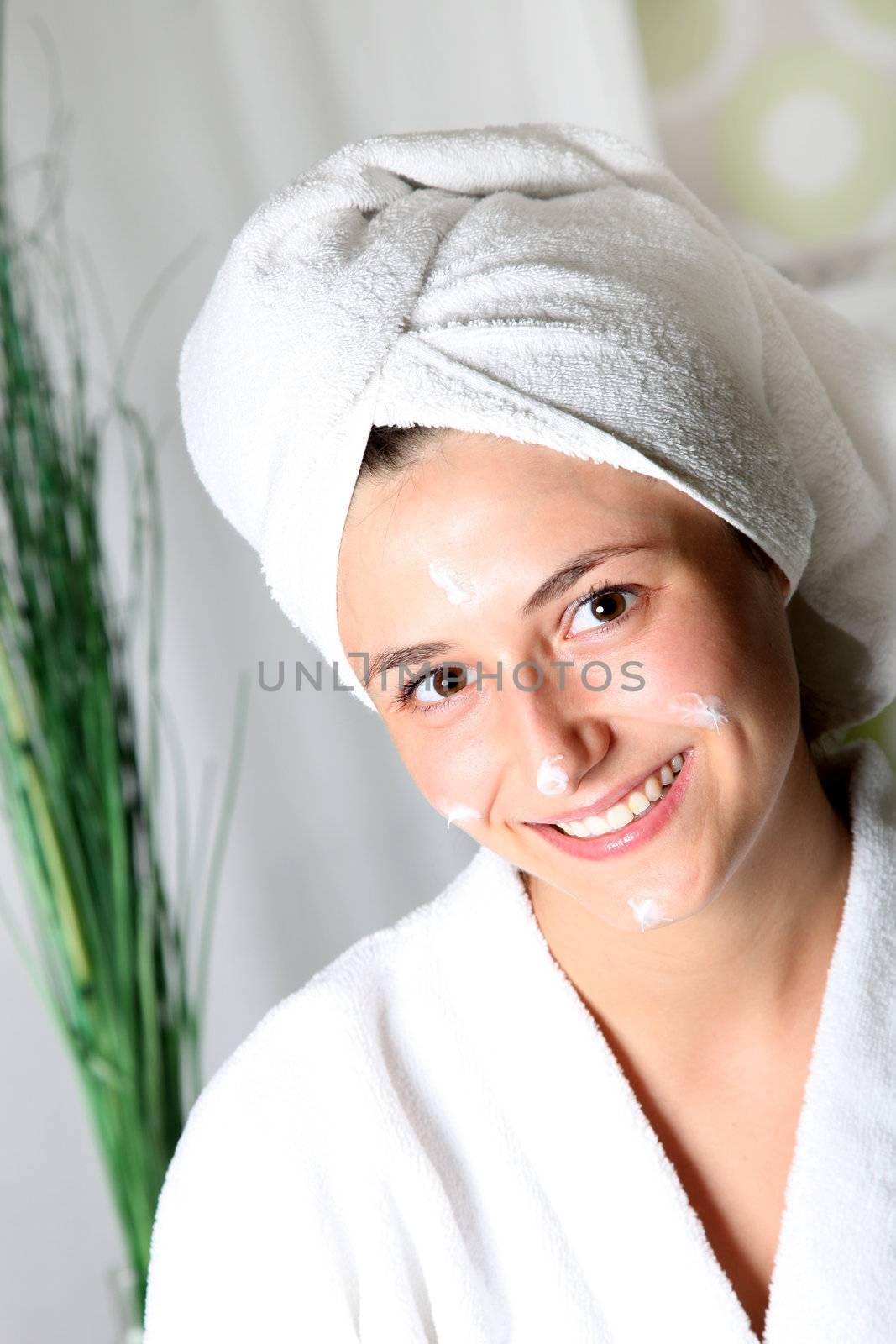 Smiling young woman with cream on her face relaxed. She wears a towel on his head and a bathrobe

