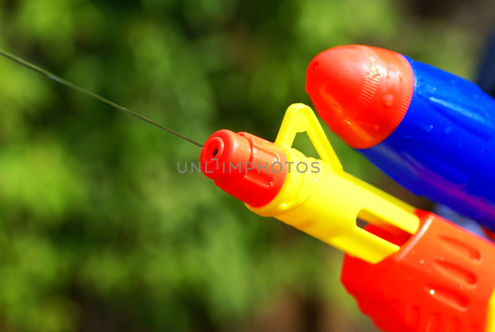 Close up of a water pistol in front of green bushes.