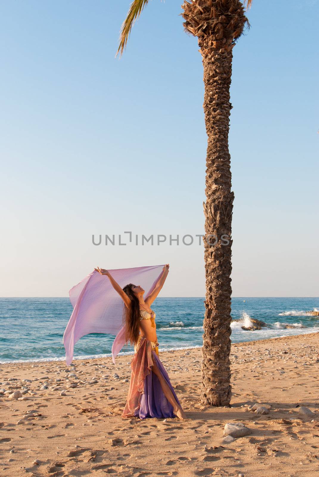 Oriental dancer with fluttering headscarf on beach setting