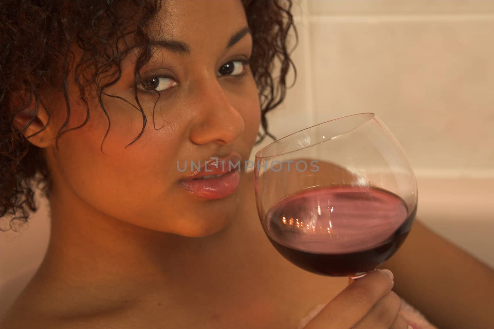 Woman enjoying a glass of red wine in the bathtub by candle light
