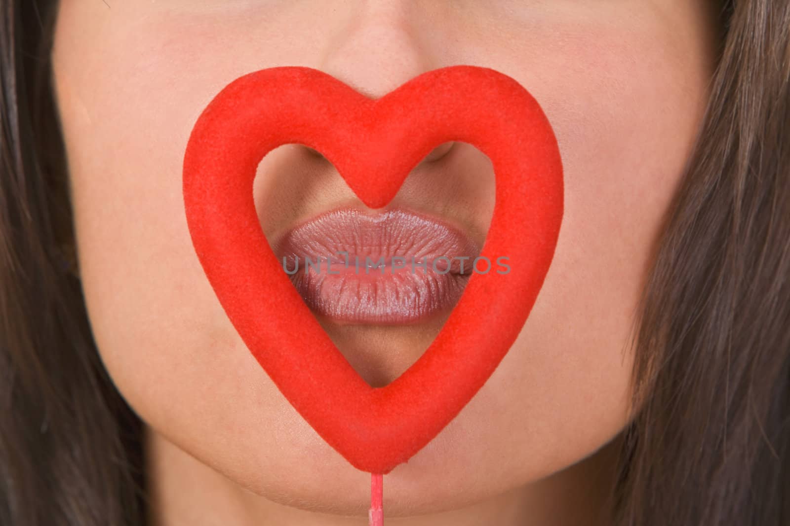 Close-up of woman lips kissing through a red heart shape.